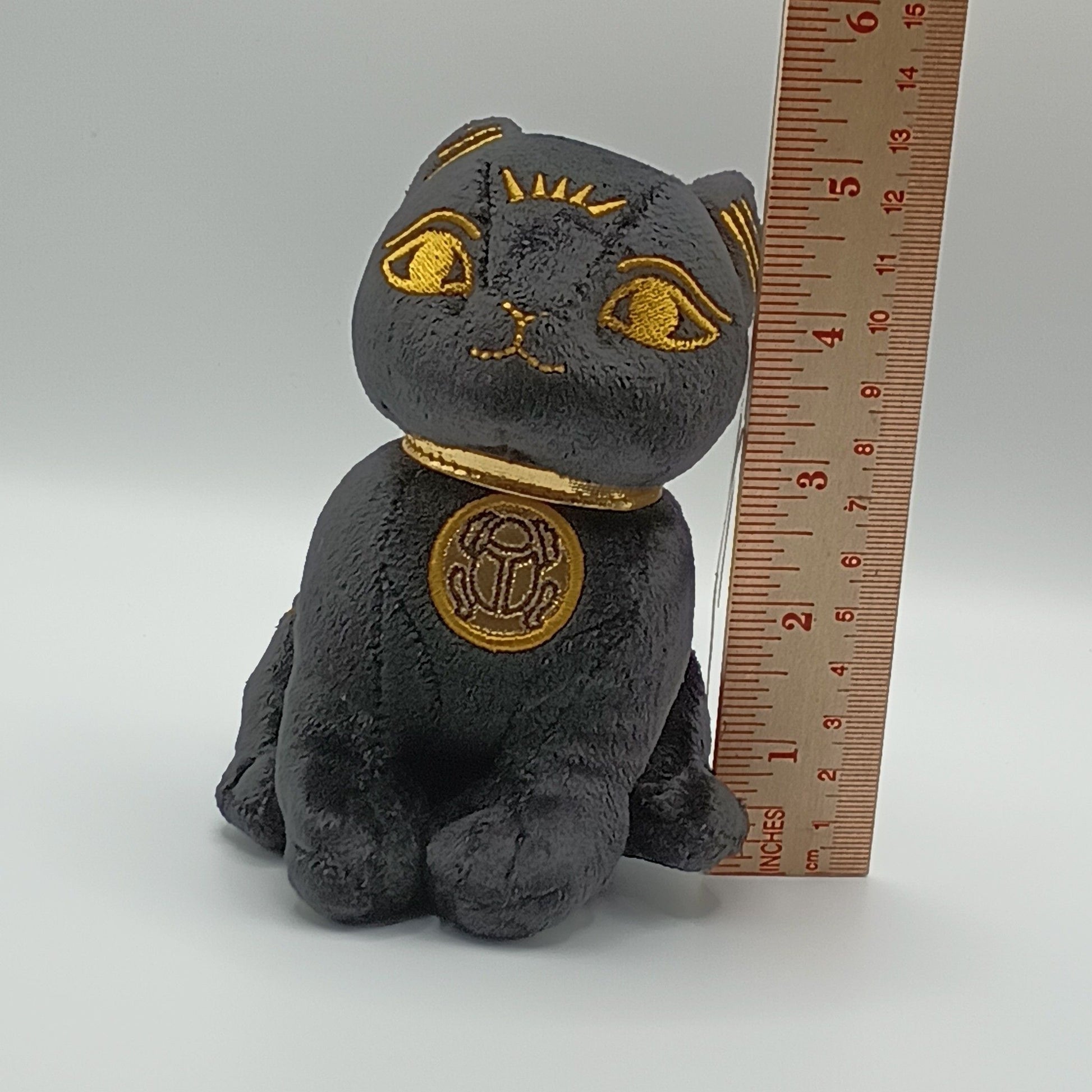 Plush Bastet cat toy with gold accents next to a ruler on a white background; approx 5 inches tall.